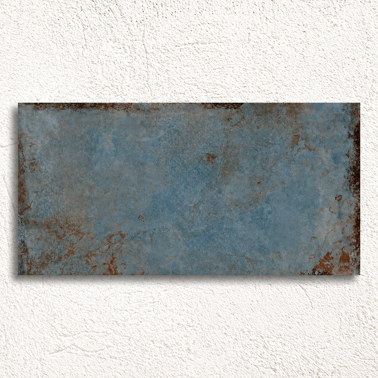 Rectangular Alloy Azzurro tile displayed against textured white plaster, showing weathered edges and mottled steel-blue colour.
