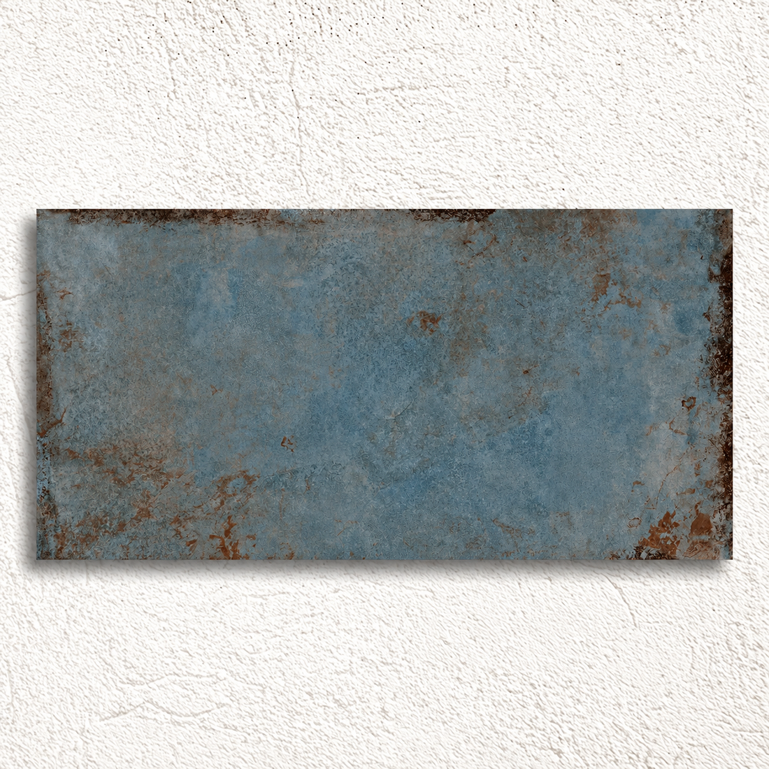 Rectangular Alloy Azzurro tile displayed against textured white plaster, showing weathered edges and mottled steel-blue colour.