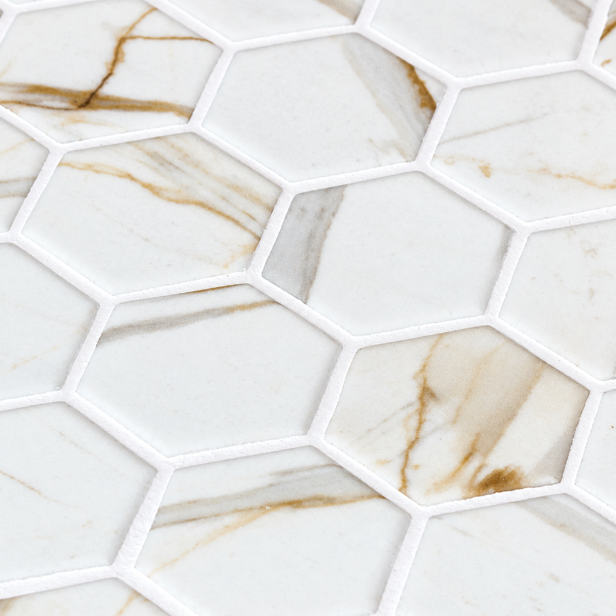 Close-up of Calacatta Gold matt glass hexagon mosaics with grey and gold veining and white grout.