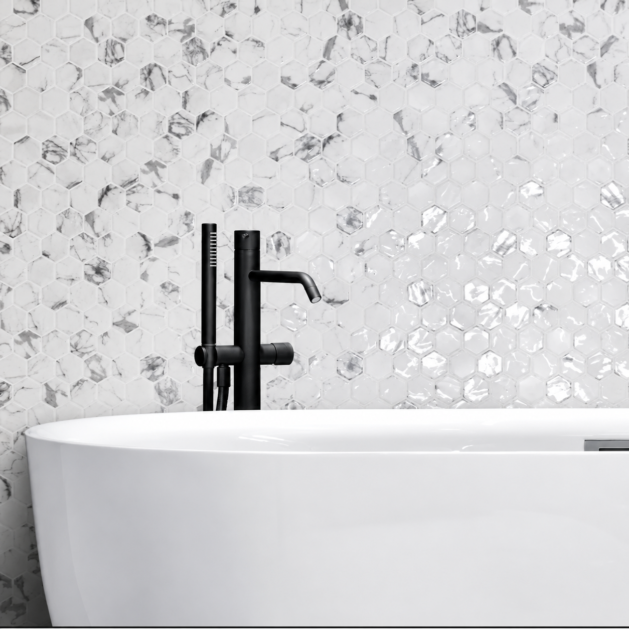 Hex XL Fosco white and grey marble-effect hexagon mosaic wall behind a freestanding bath with black tap.