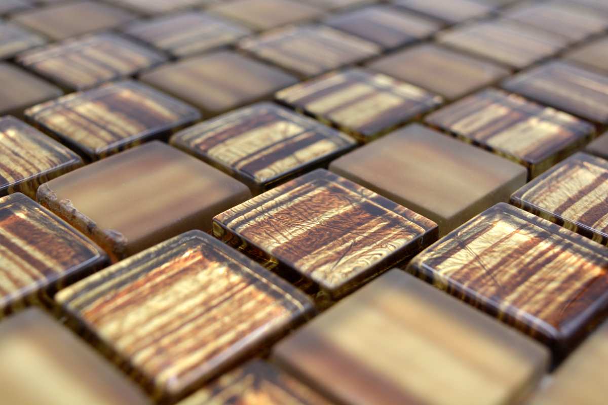 Macro image of glossy honey bronze glass mosaic chips with warm amber variation, linear streaking and polished reflective finish