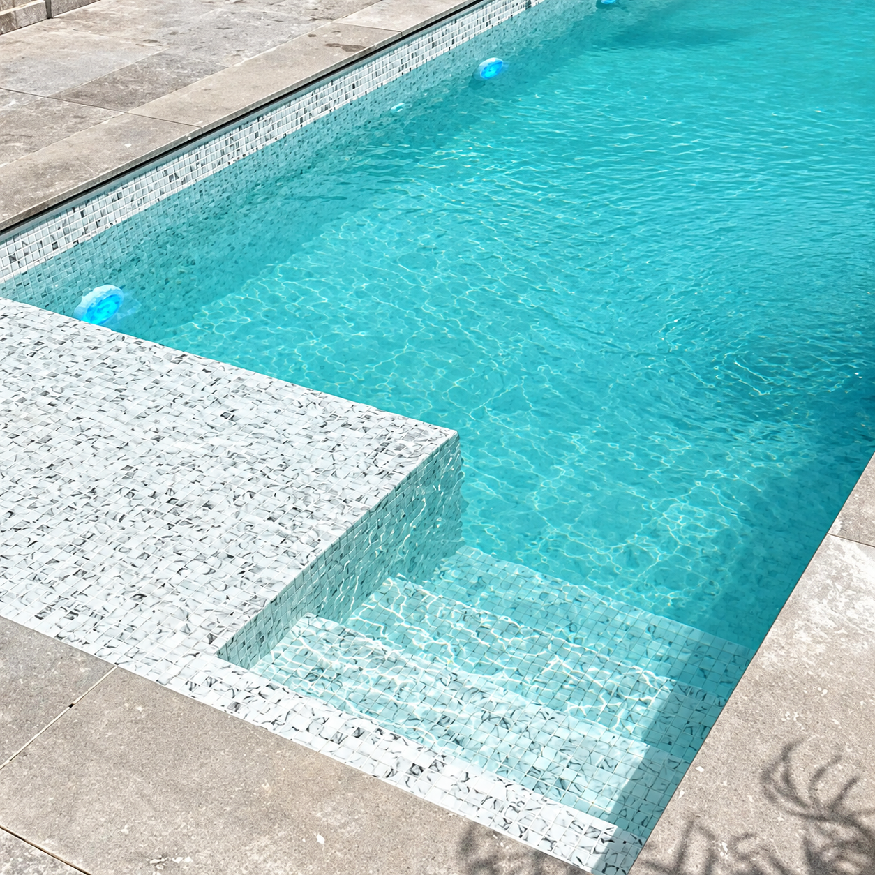 Karma Calacatta white marble effect glass mosaics lining a swimming pool with submerged steps and turquoise water.