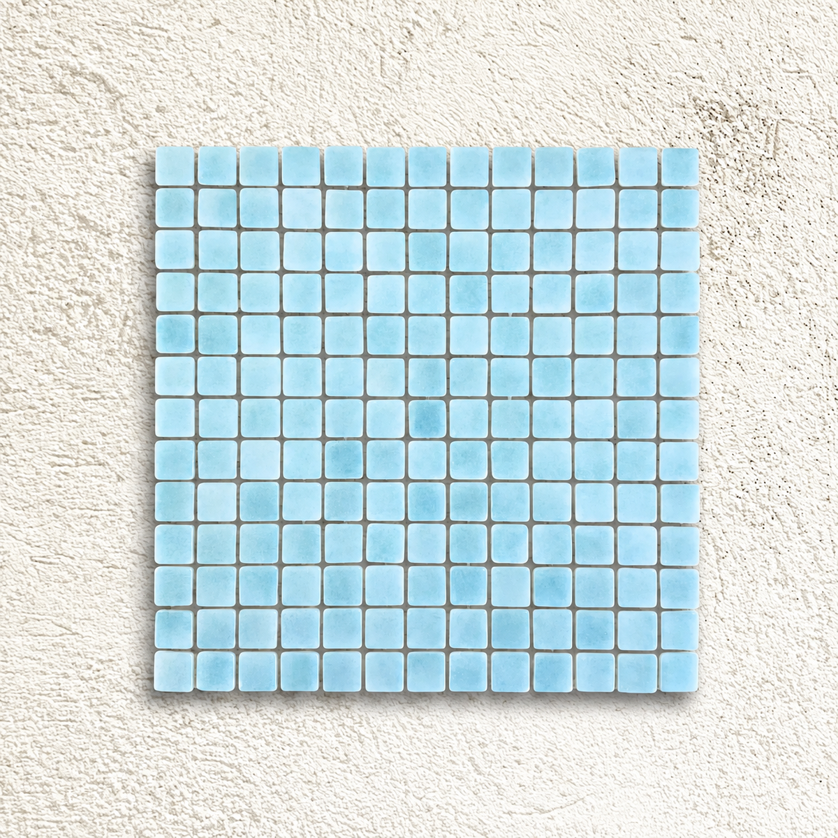 Niebla Foggy Aqua glass mosaic sheet with pale aqua blue square tiles on a white textured background.