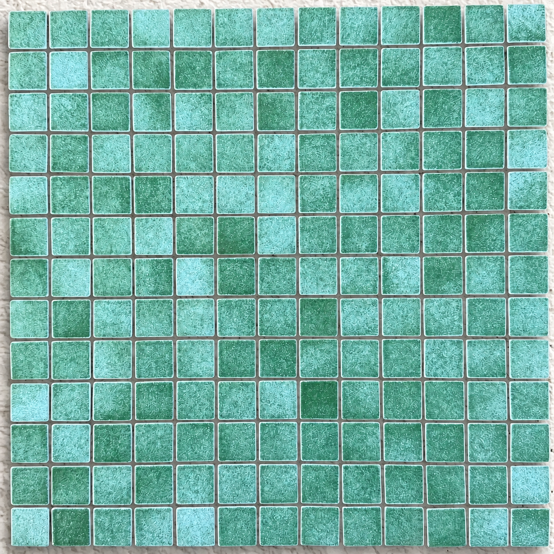 Close-up of Niebla Giava glass mosaic tiles showing sea-green tones, fine mottling and evenly spaced square pieces.