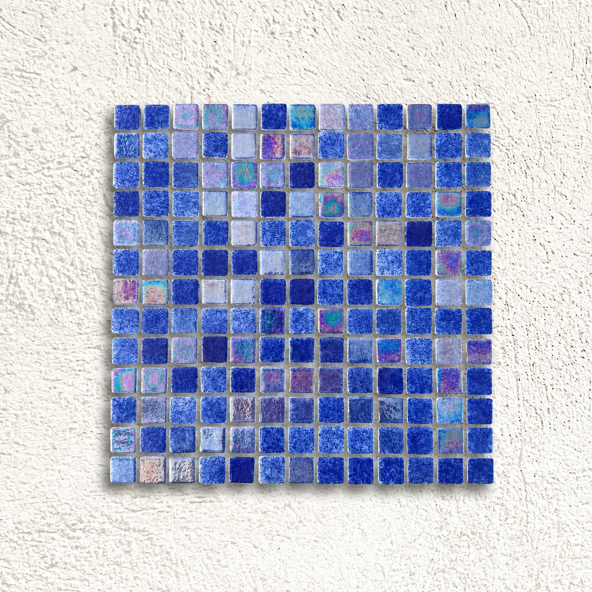Niebla Mix-Iris Urola blue glass mosaic sheet with cobalt, pale blue and iridescent square tiles against a white textured background.