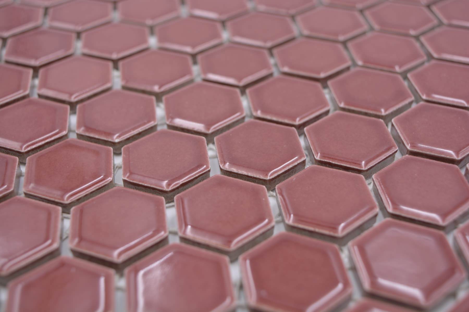 Shapes gloss burgundy red ceramic hexagon mosaic with subtle rose tones and visible mesh between tiles.