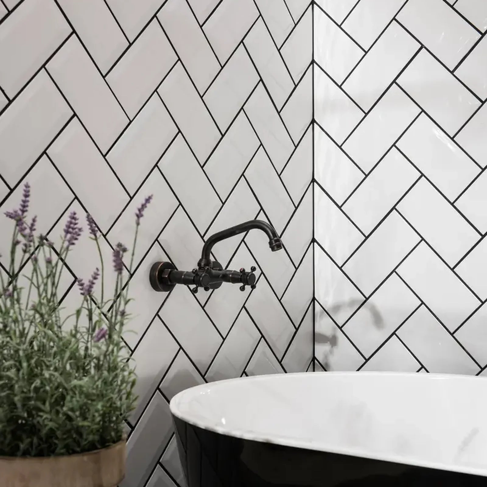 Classico Blanco White Metro 100x200mm gloss wall tiles installed in herringbone pattern with black grout behind freestanding bath