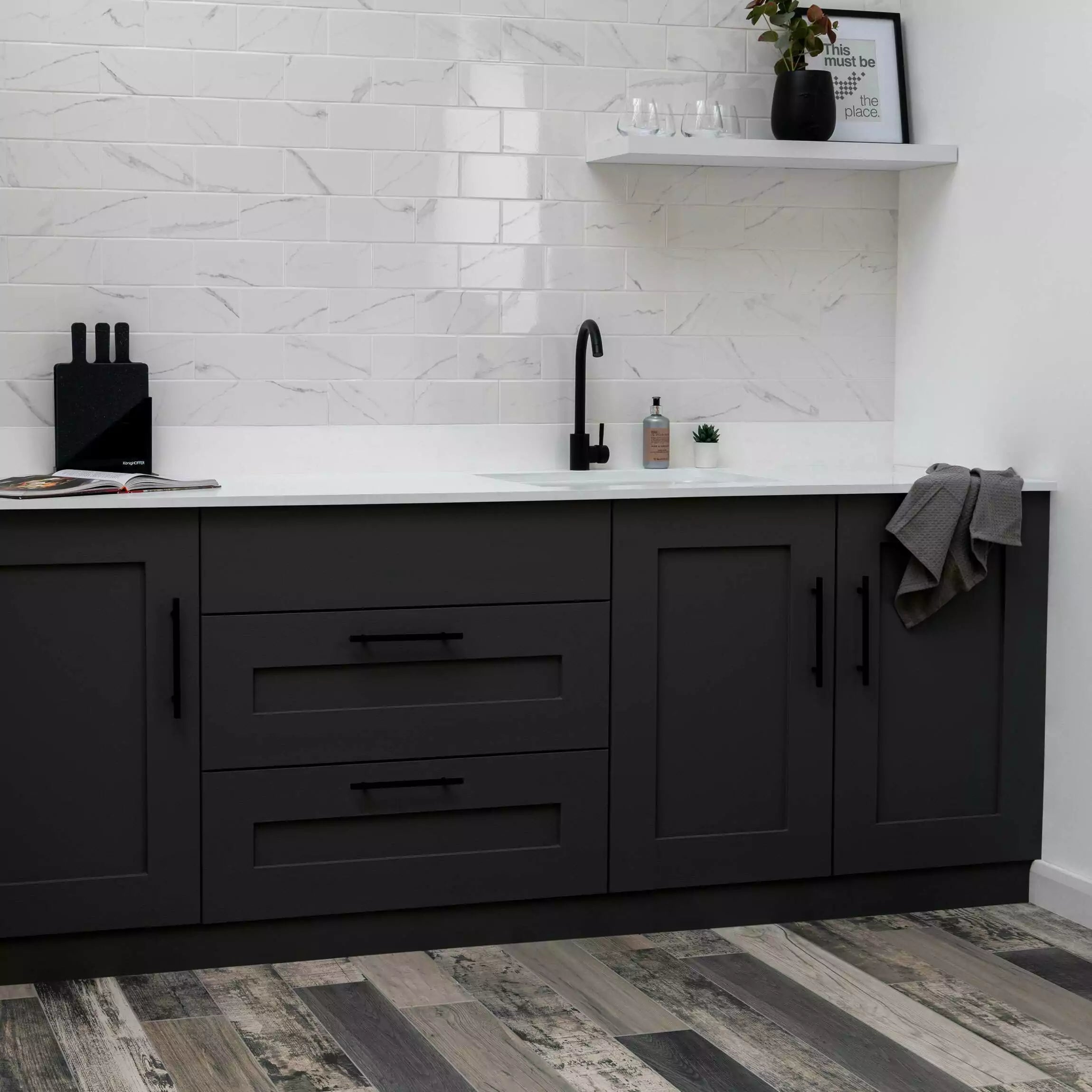 A modern kitchen scene showing dark charcoal gray cabinets with black handles, a white countertop, a white subway tile backsplash, a black faucet, and a gray towel draped over the side cabinet.